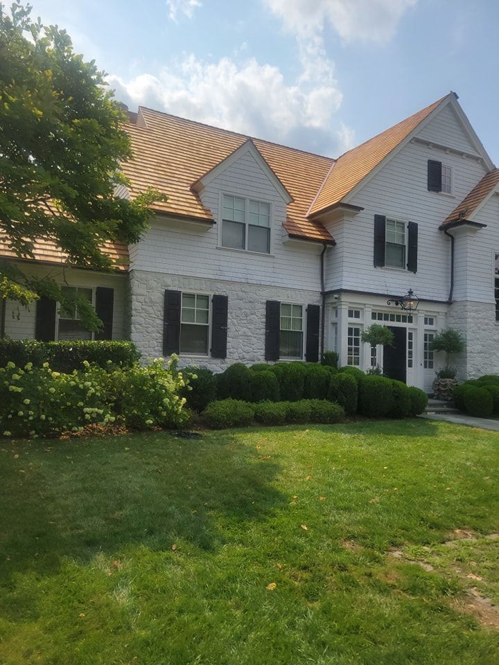 White house with light brown roof, black shutters, green lawn, blue sky.