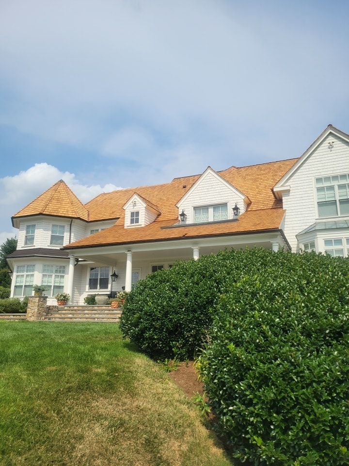 White house with a brown wooden shingle roof, green lawn, and blue sky.