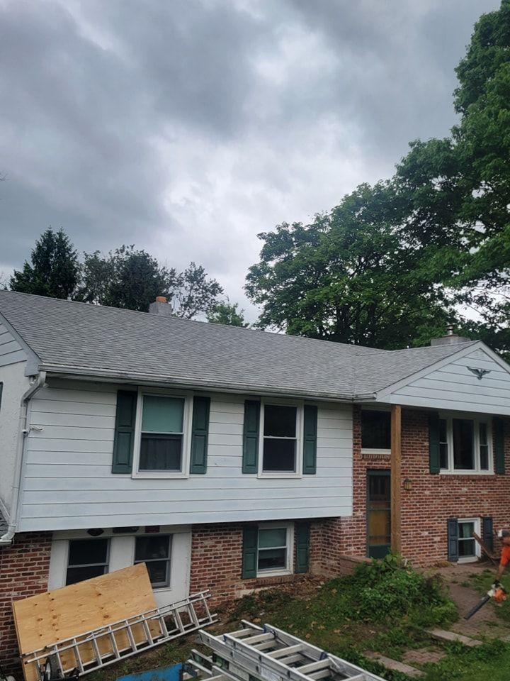Two-story house with gray roof, white siding, and green shutters under cloudy sky.