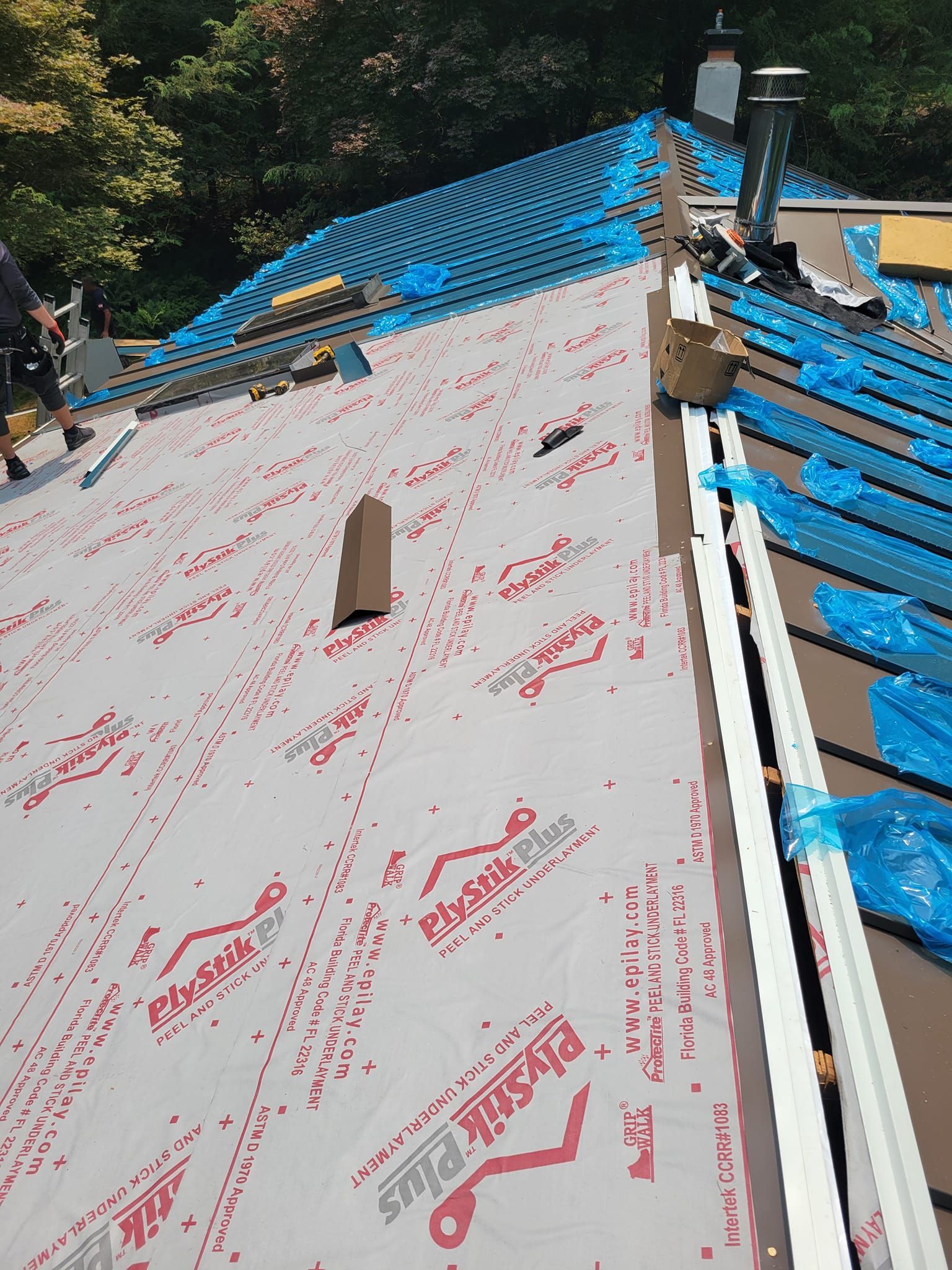 Roof being repaired with new underlayment and materials. Blue plastic sheeting covers some areas.