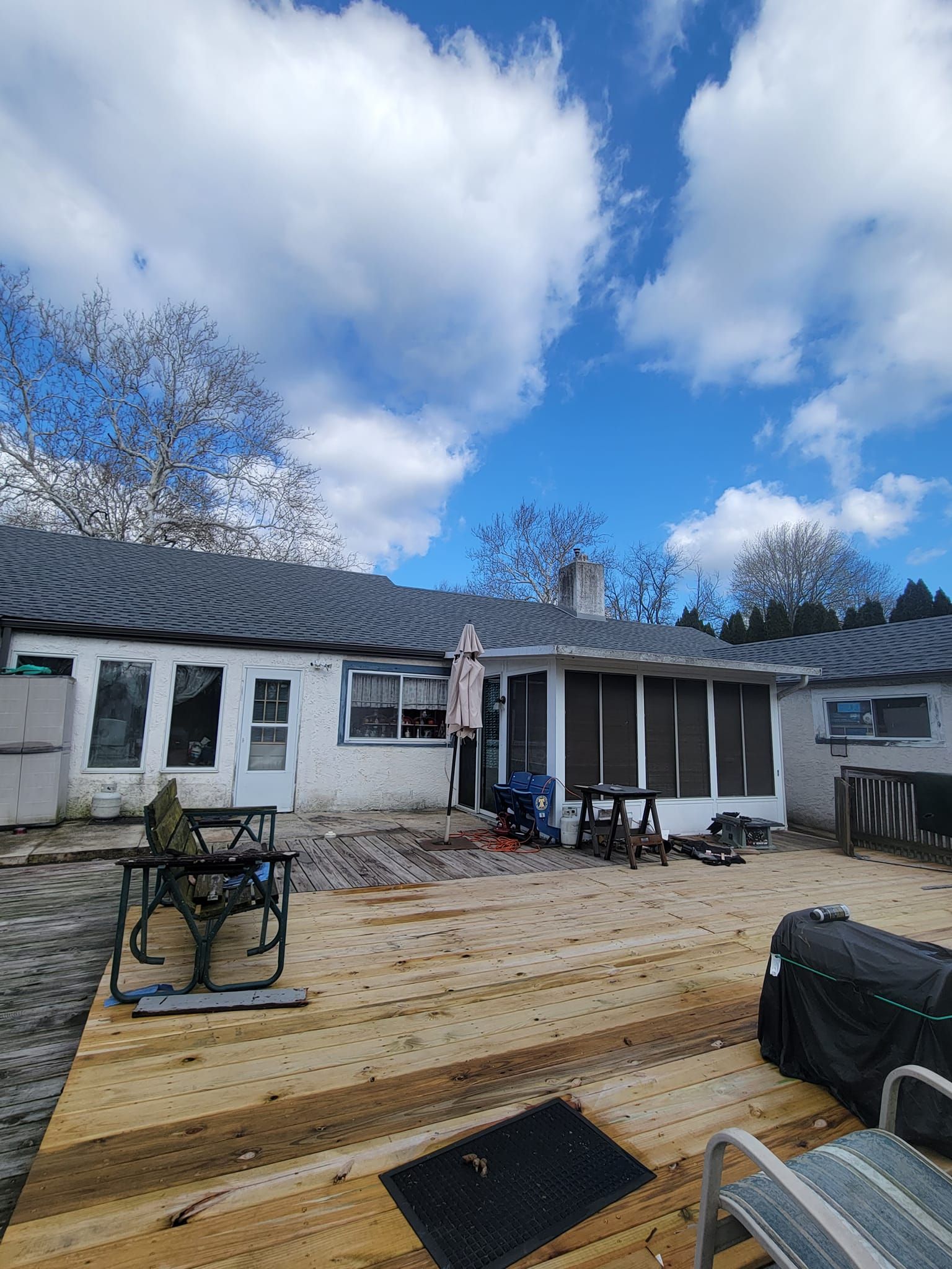 Backyard with wood deck, white house with gray roof, blue sky with clouds.