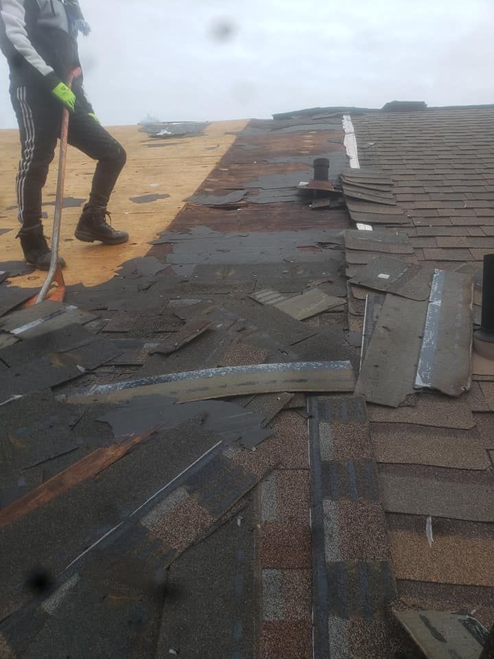 Roofer removing old shingles from a roof on a cloudy day. Visible debris and exposed underlayment.