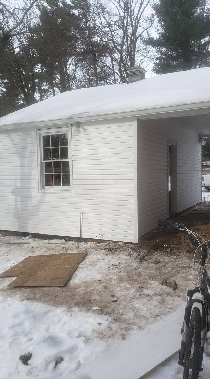 White building with snow on the ground and roof. A window and an open doorway are visible. A bicycle leans on the right.