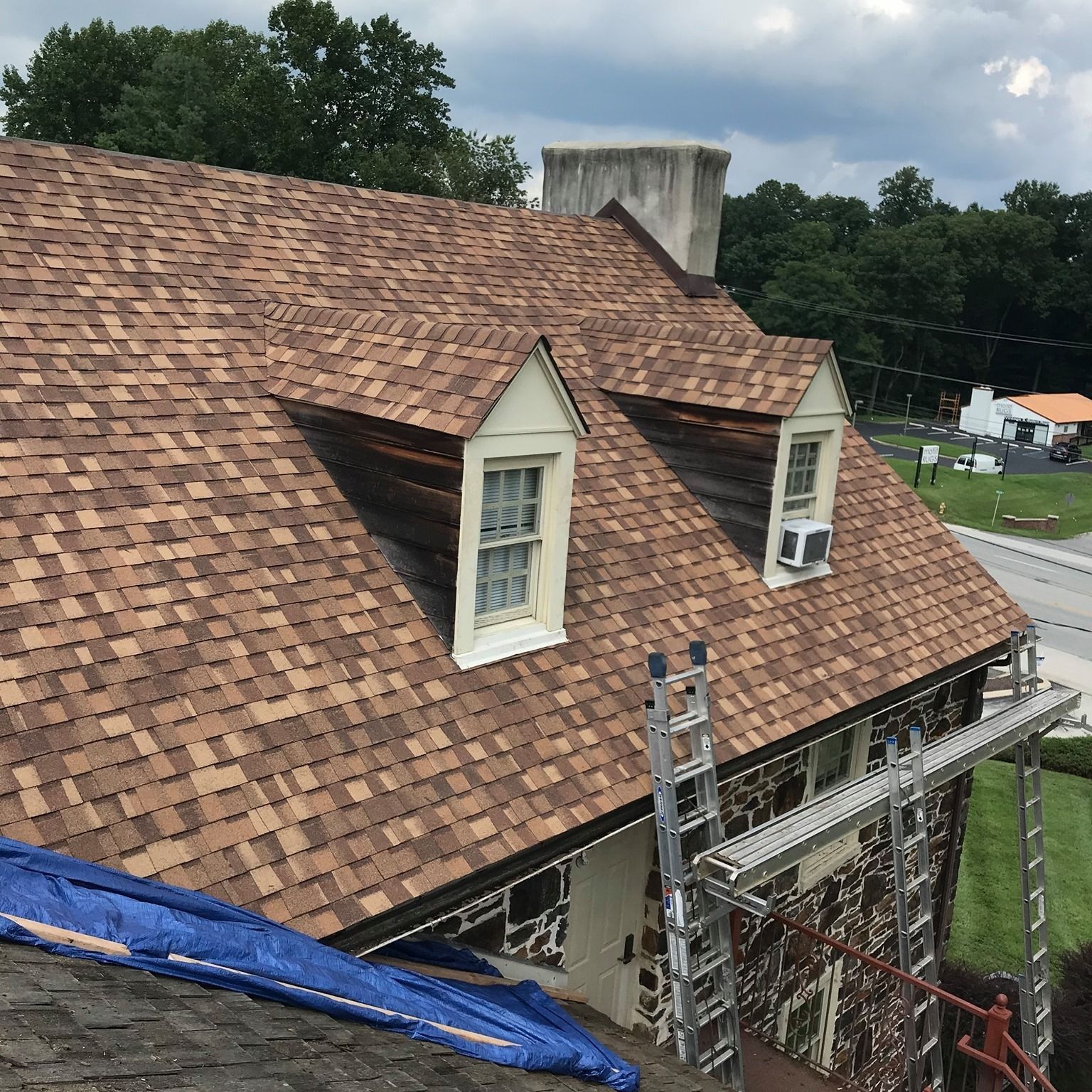 Brown shingle roof with two dormers. A ladder and scaffolding are set up for roof work.