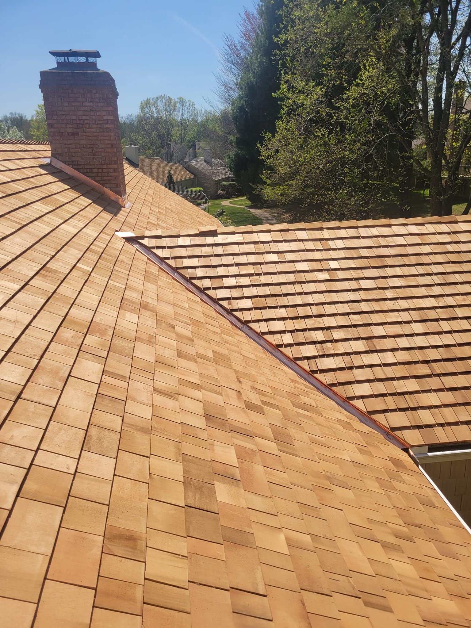Brown cedar shake roof with brick chimney, sunny outdoor setting.
