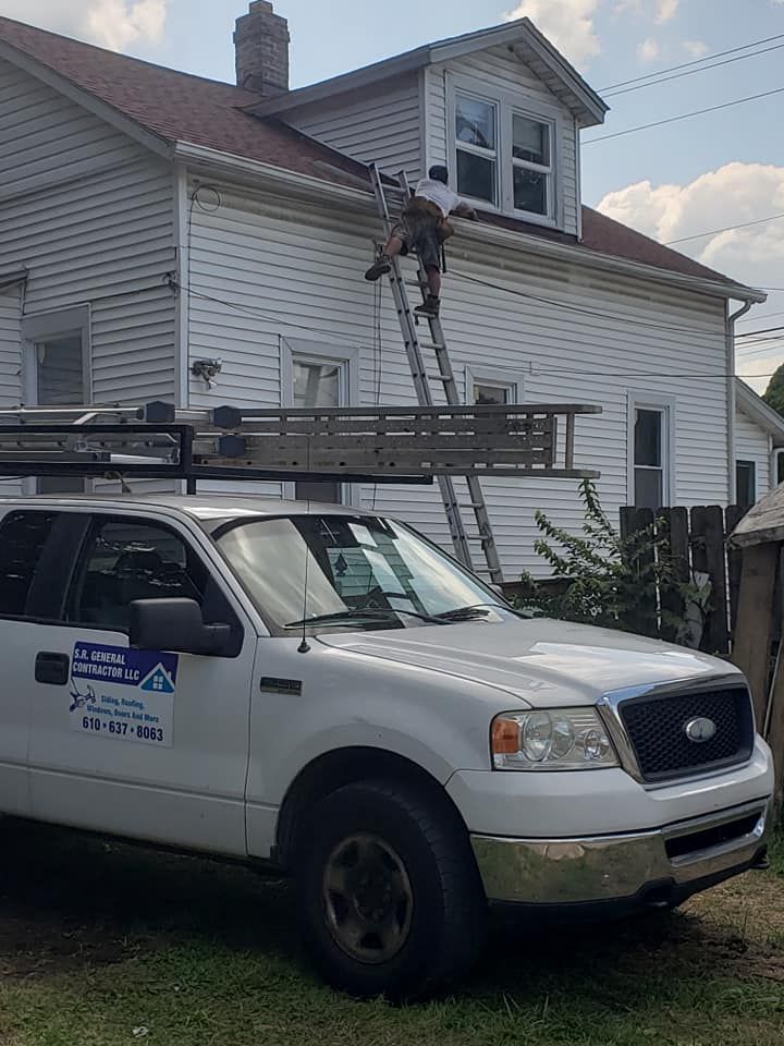 White truck parked next to a house with a person on a ladder working on the roof.