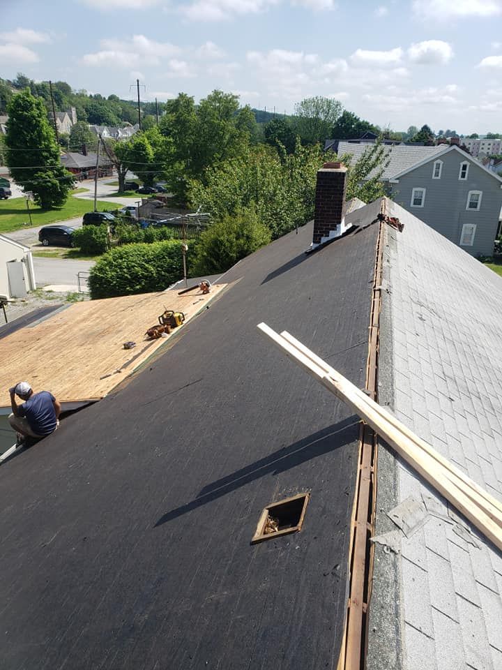 Roofer working on a house roof. Dark asphalt shingles are installed, next to the grey ones, on a sunny day.