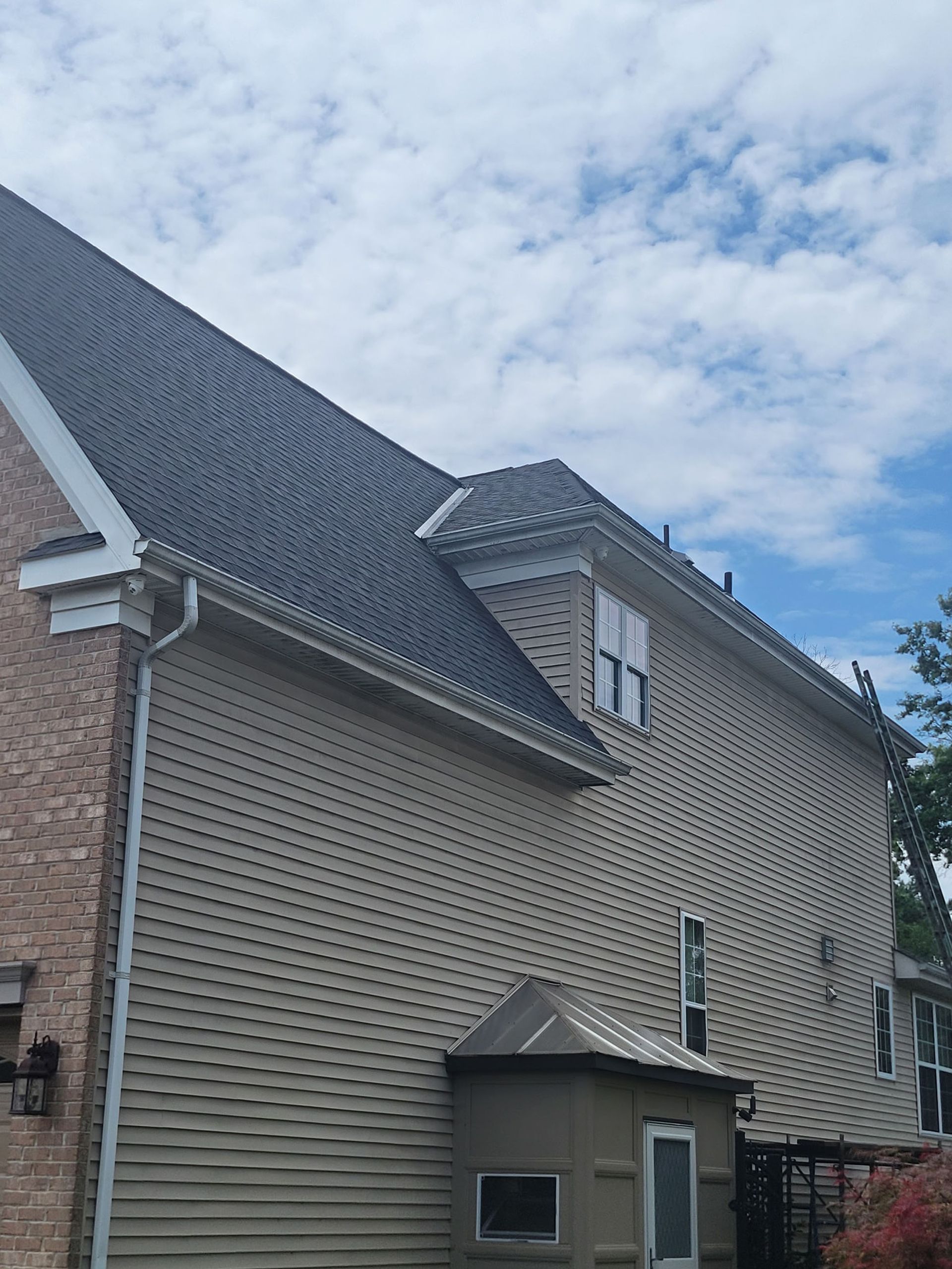 Beige house with gray roof and brick siding, against a cloudy sky.