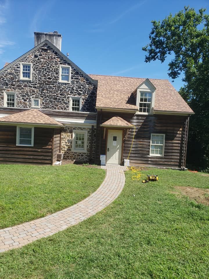 Stone and log house with a brick path leading to the front door, under a blue sky.