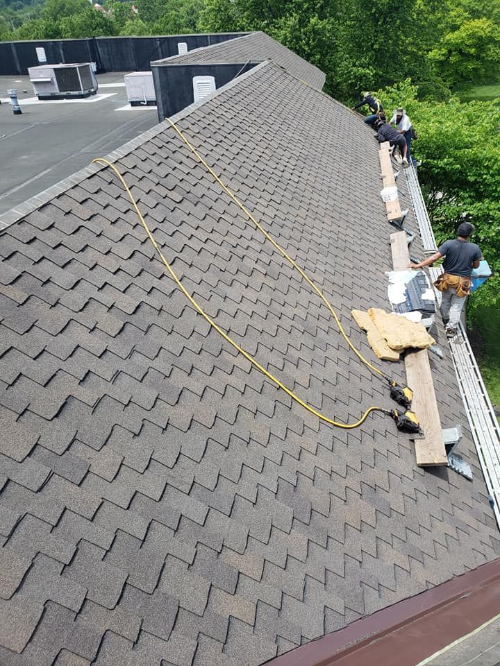 Roofers working on a shingled roof, brown shingles, tools and materials present, sunny day.