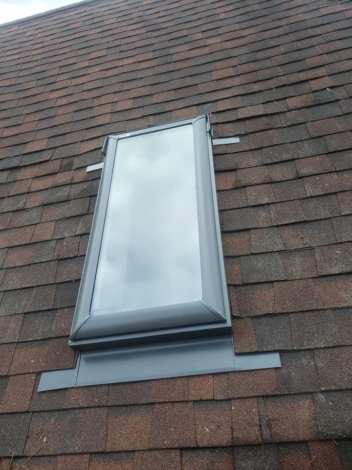 Skylight on a brown shingle roof, surrounded by gray flashing.