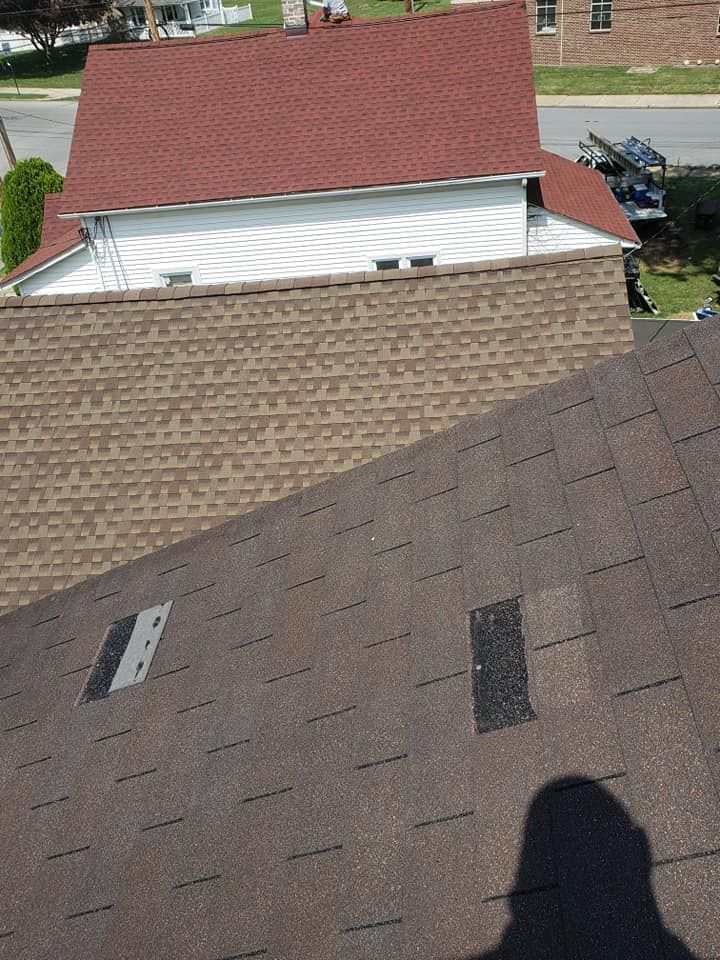 Overhead view of a brown shingled roof with two patches, partially covering a house with a red roof.