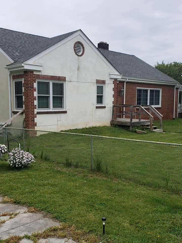A one-story house with a brick exterior and a small wooden porch, viewed from the front yard.