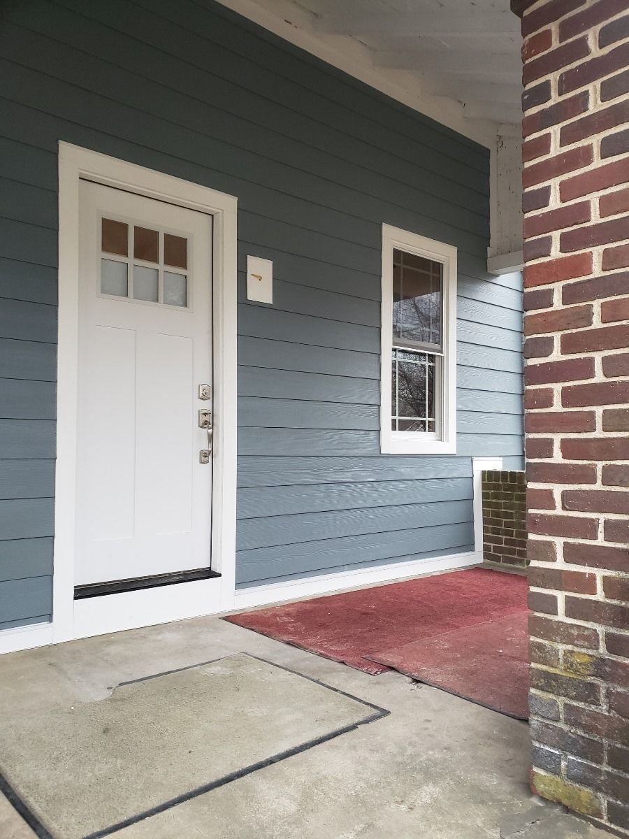 White door with glass panes and a small window on a blue-sided porch with a brick pillar.