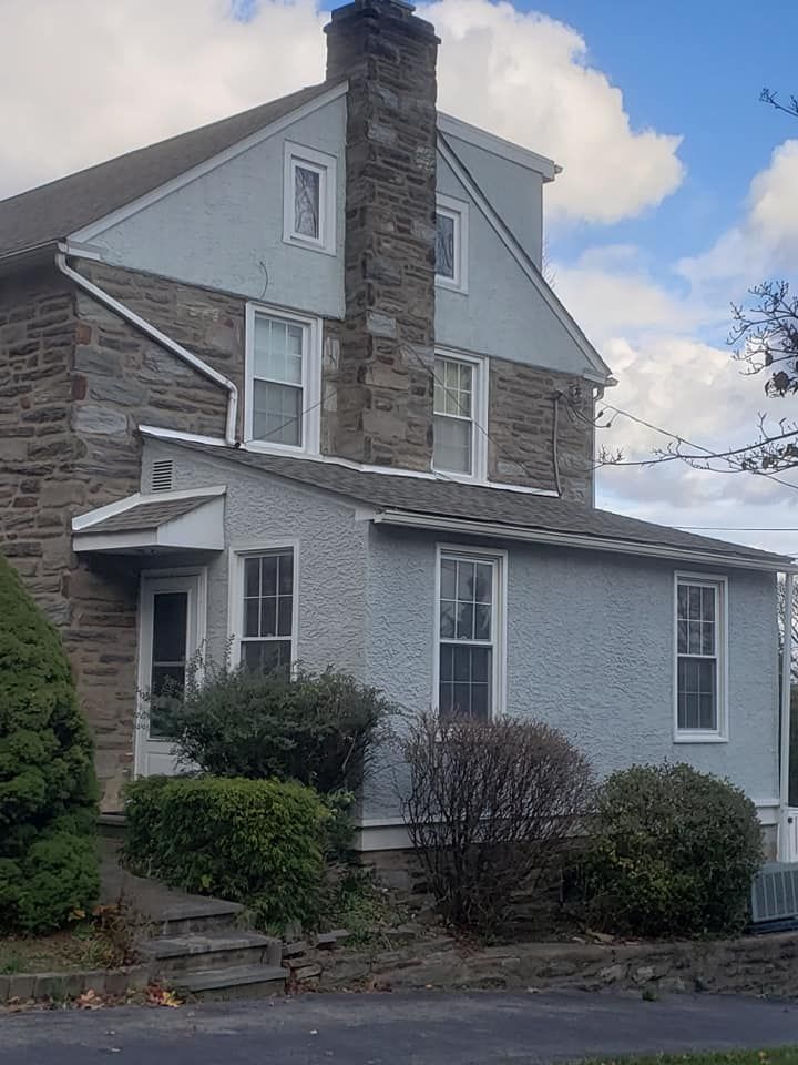 Two-story house with stone and stucco exterior, chimney, windows, and bushes in front.