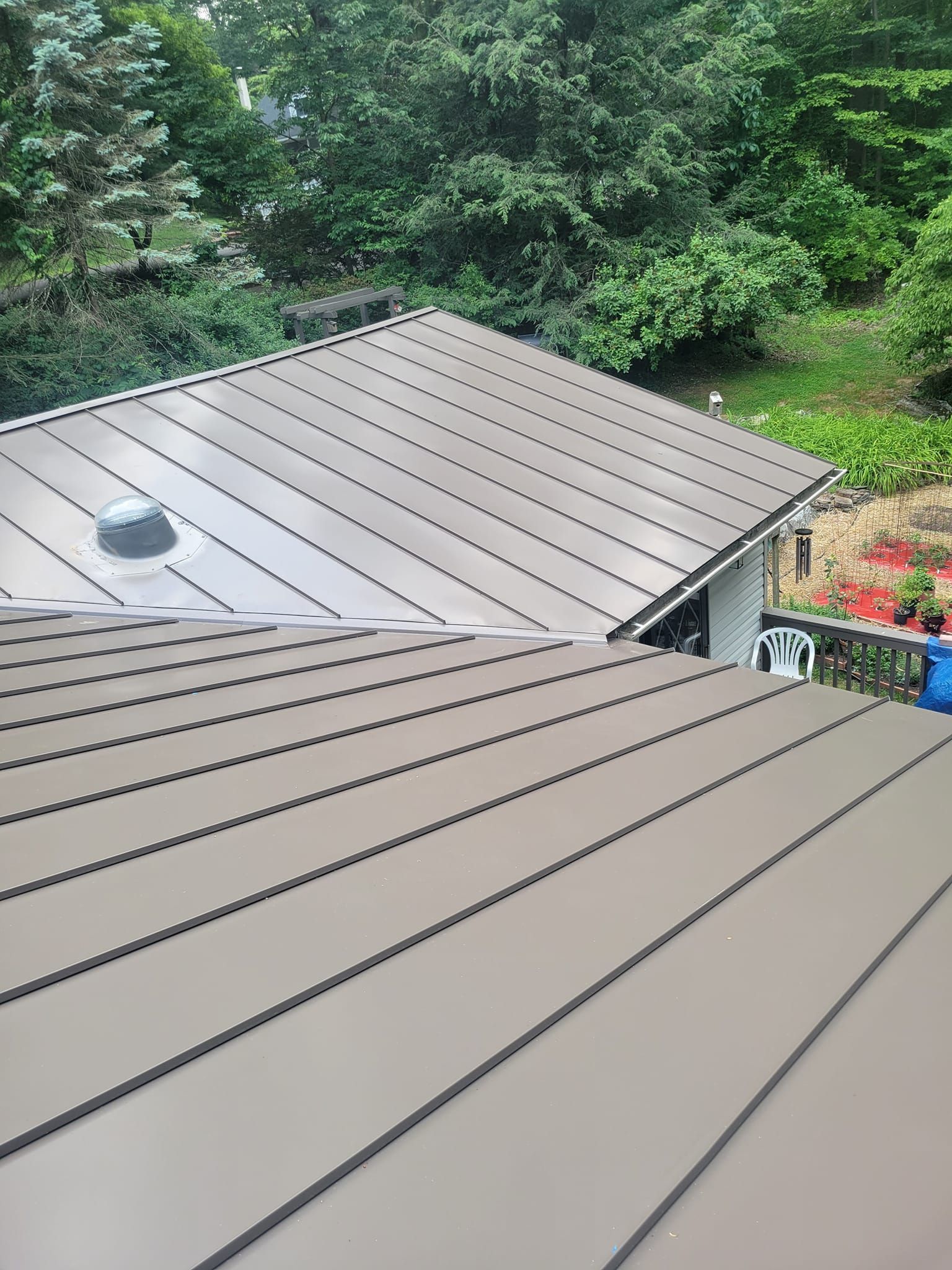 Metal roof with dark ridges, sloped and set against a green tree-filled background.