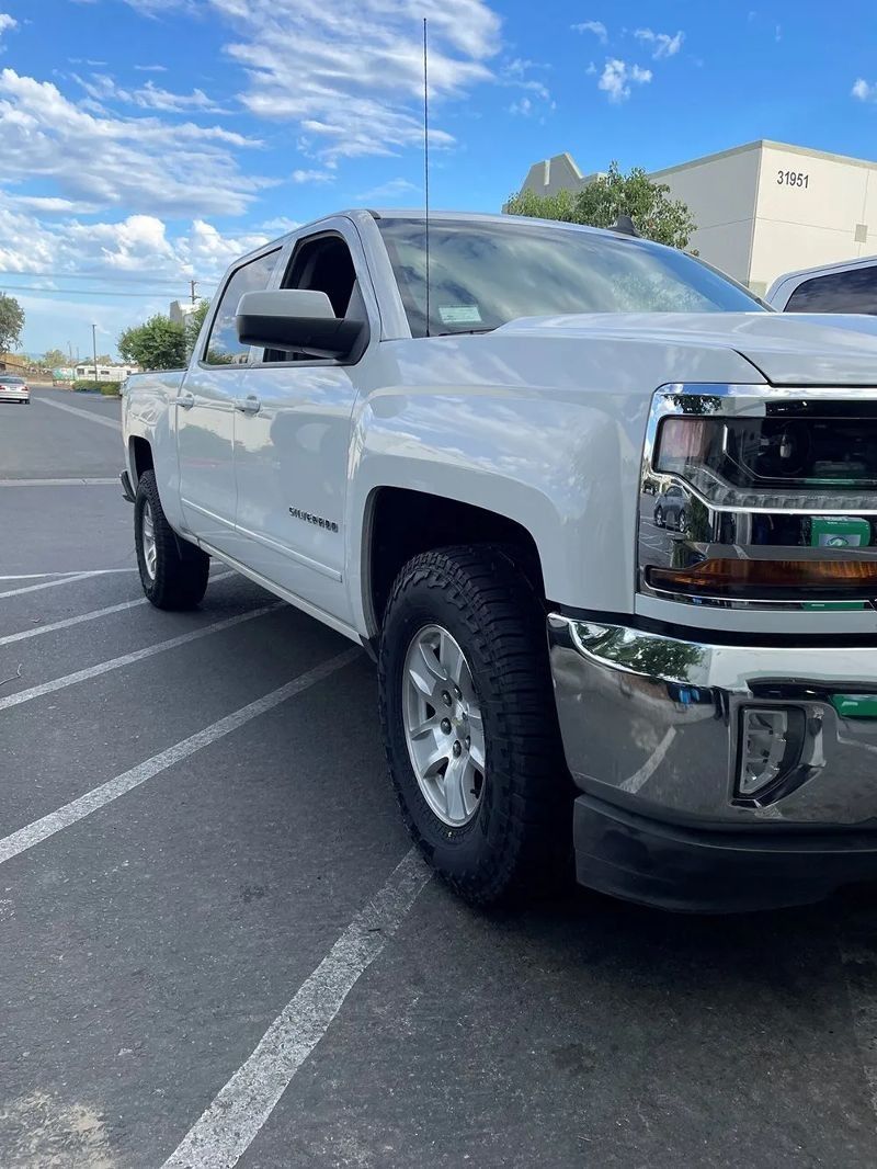 White Chevrolet pickup truck parked on asphalt. Clear blue sky.