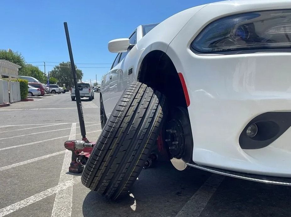 White car with flat tire being lifted by a jack outdoors.