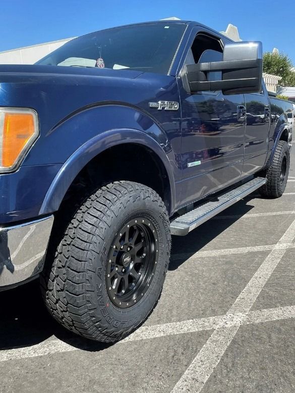 Blue Ford F-150 truck with black wheels parked on an asphalt surface.