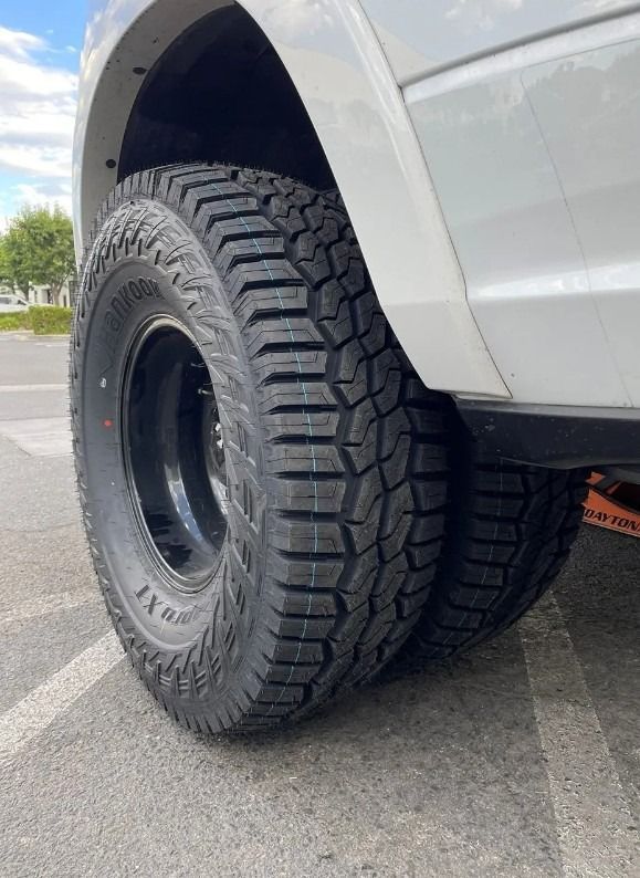Close-up of a white dually truck with black rims and rugged tires. The tires are outdoors on pavement.