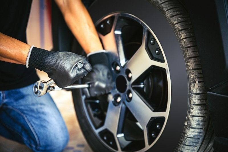 Person wearing gloves uses a wrench to loosen lug nuts on a car tire.