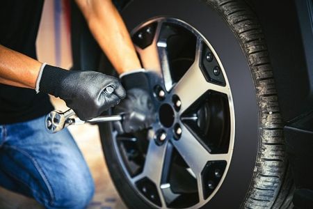 Person wearing gloves uses a wrench to loosen lug nuts on a car tire.