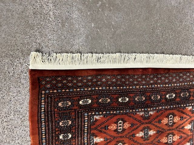 A rug with fringe is sitting on a gray carpet.
