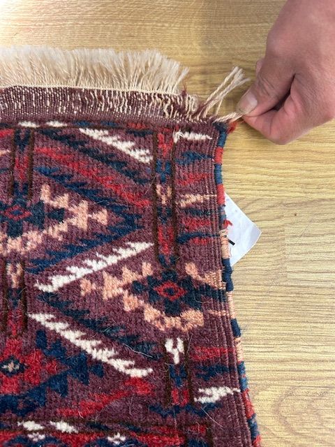 A person is holding a piece of rug on a wooden table.