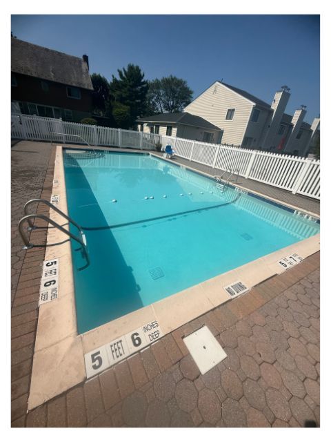 Pool with blue water and depth markers, surrounded by white fence and brick deck