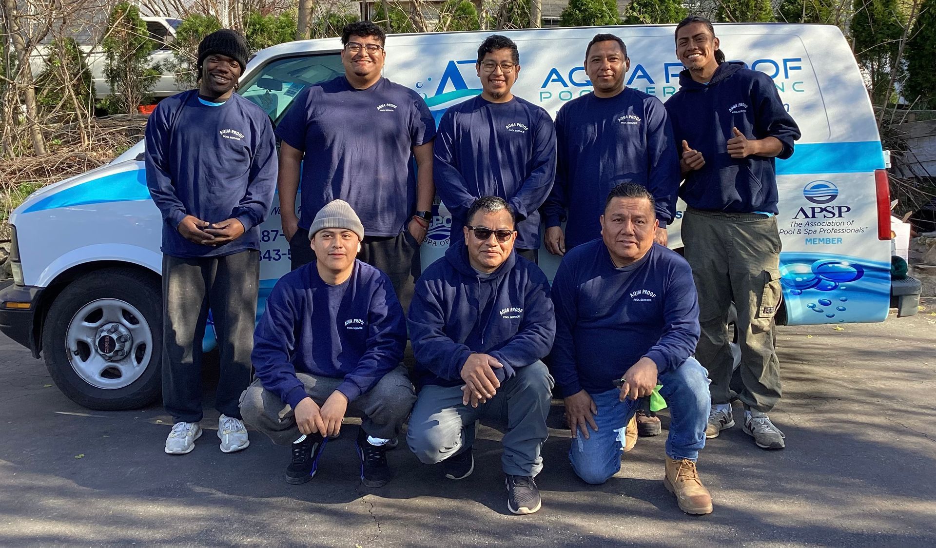 A group of men in blue shirts pose in front of a white van with Aqua Proof logo