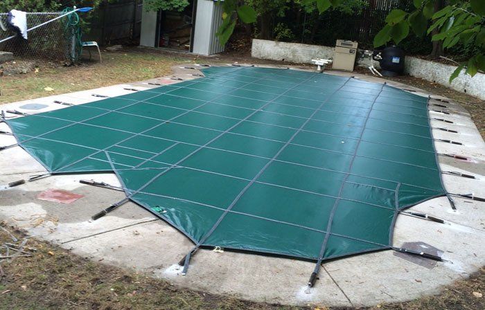 Green pool safety cover stretched over a concrete patio