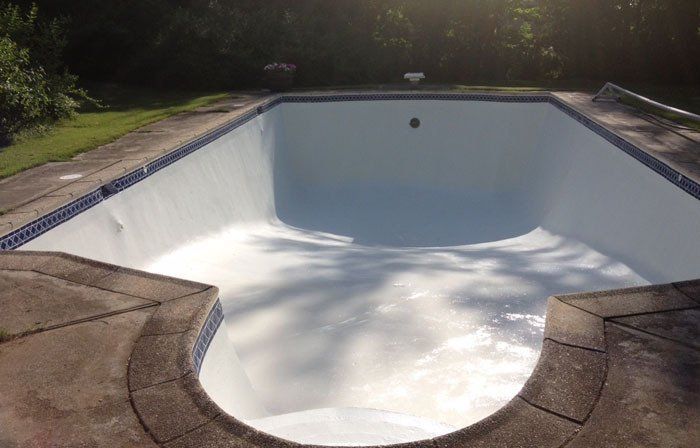 Empty, light blue painted swimming pool in an outdoor setting, with stone edges and green grass