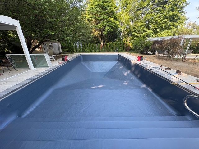 Empty rectangular pool with dark blue interior, steps, and a stainless steel handrail
