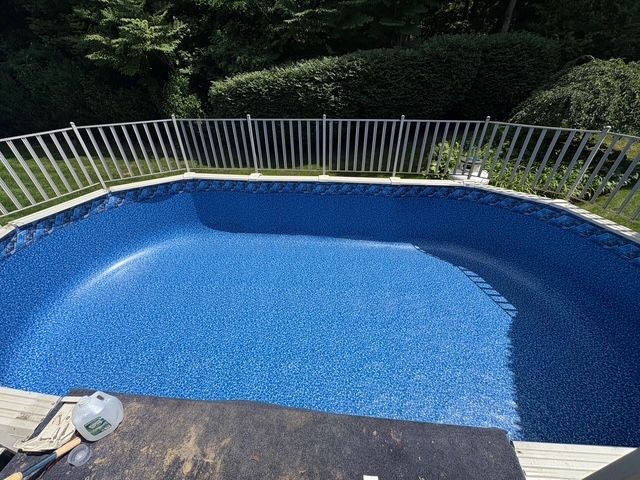 Empty blue-lined swimming pool with a white fence around the edge, surrounded by greenery