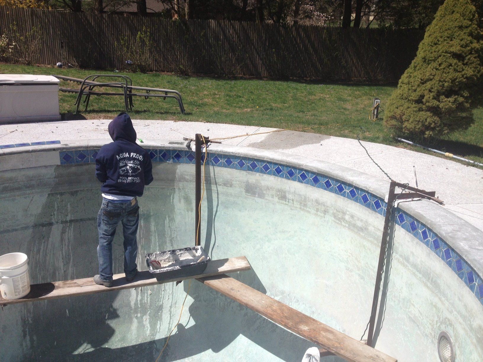 Person in hoodie standing on wooden planks inside an empty pool, preparing for maintenance