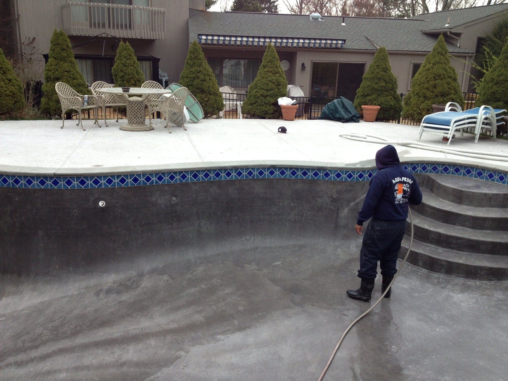 Man cleaning an empty pool in a backyard, snow on the patio furniture