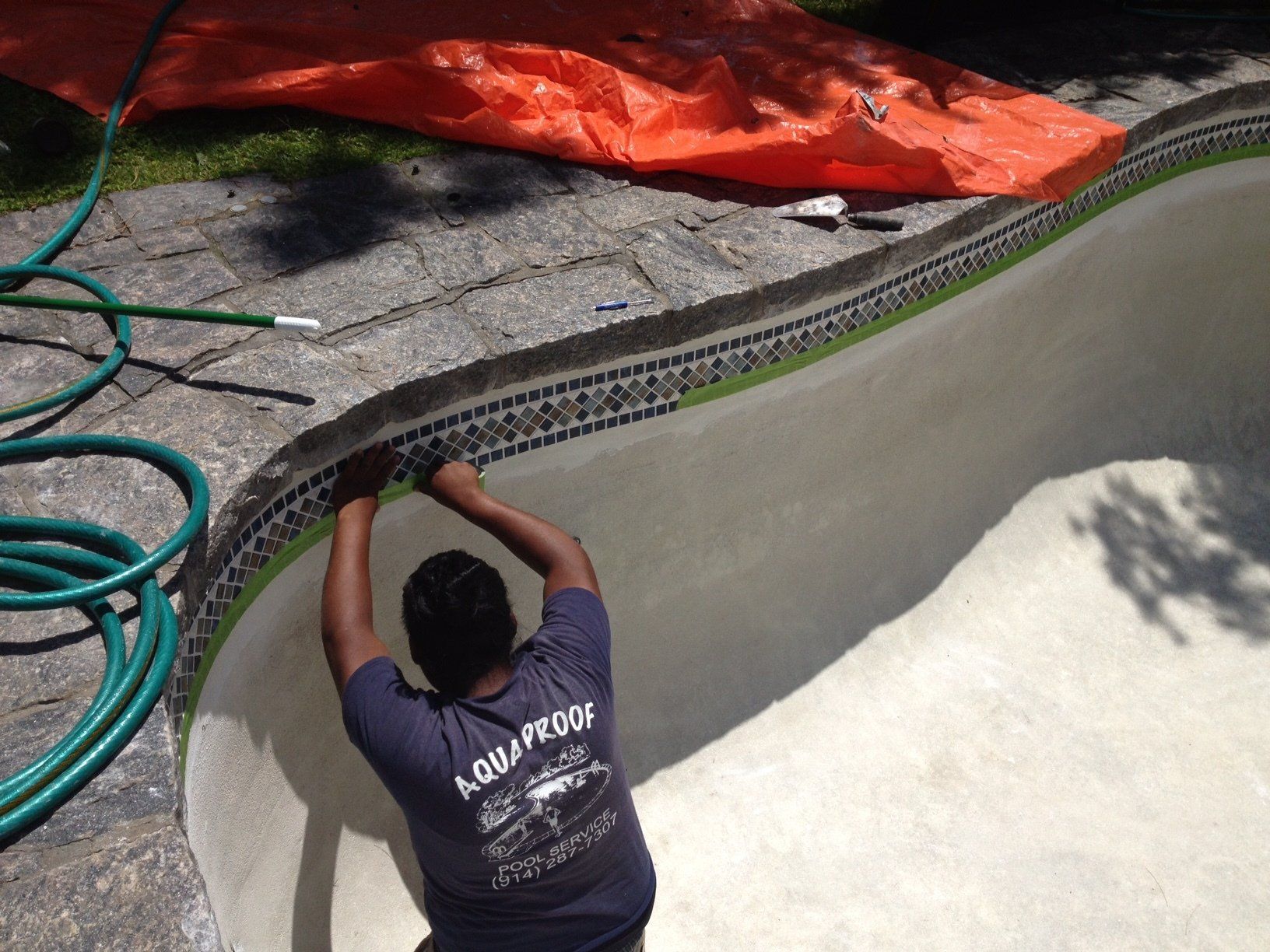 Man applying tile to the edge of an empty swimming pool