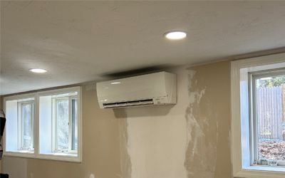 A room with a wall mounted air conditioner and two windows.