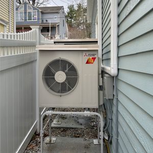 A large air conditioner is sitting on the side of a house next to a white fence.