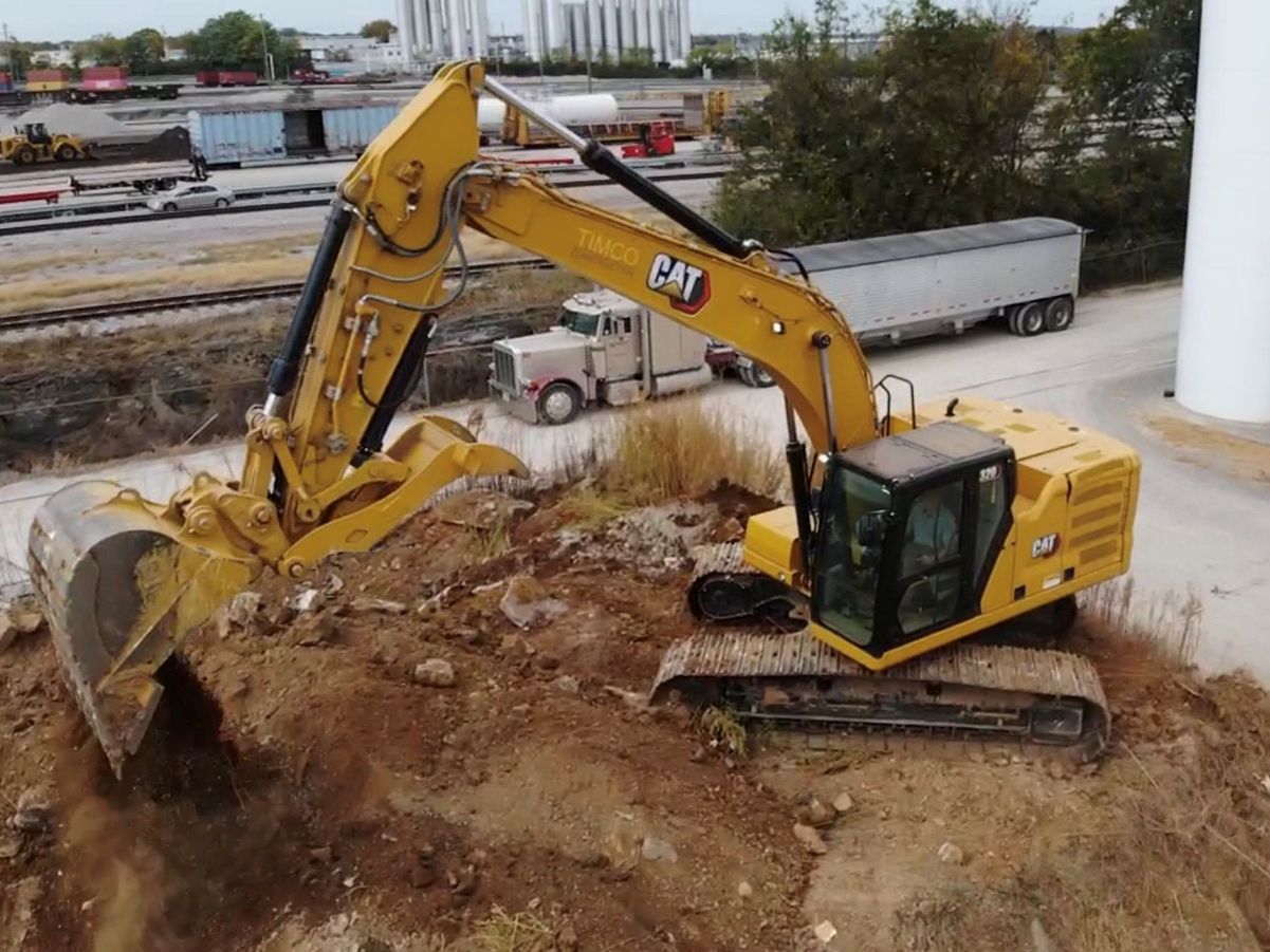 A yellow cat excavator is digging a hole in a dirt field.
