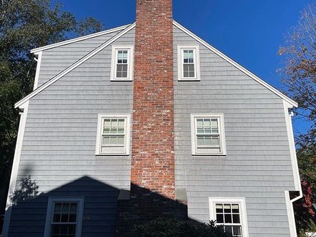 A large gray house with a red brick chimney