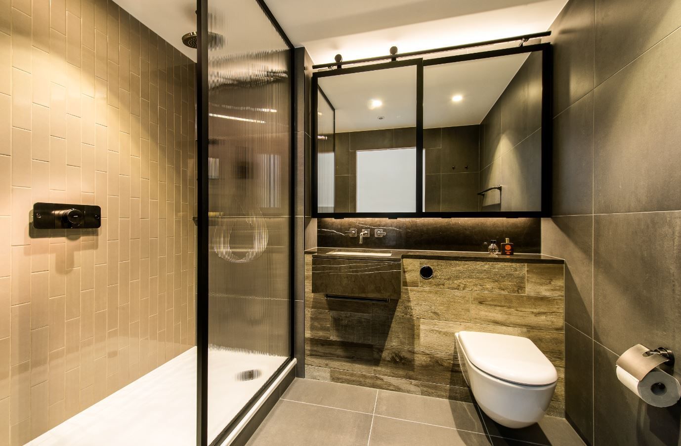 Modern bathroom with shower, toilet, and vanity. Gray tile walls, black framed mirror, and fixtures.