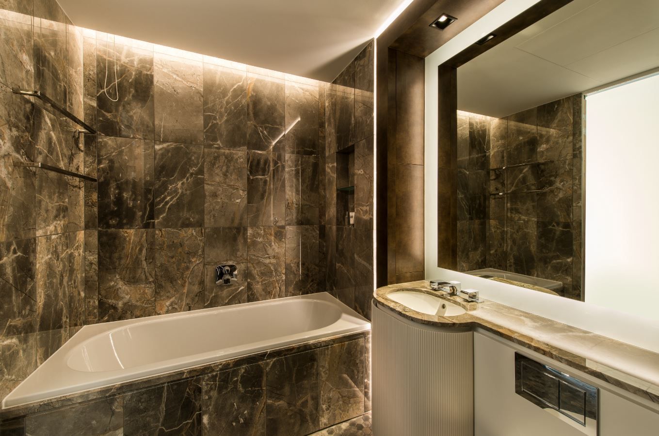 Luxury bathroom with marble tile, bathtub, and a large mirror. Soft lighting enhances the dark hues.