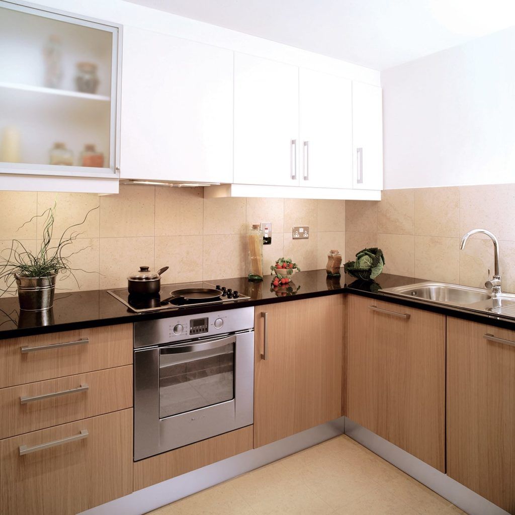 Modern kitchen with light wood cabinets, white upper cabinets, stainless steel oven, black countertop, and sink.