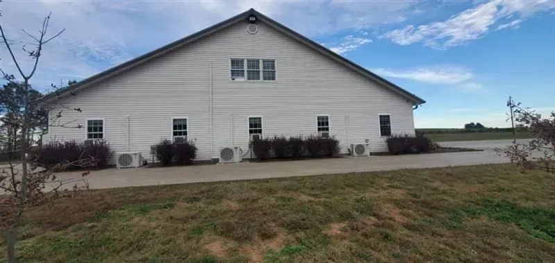 White building with a gabled roof. Air conditioning units are below windows. Green grass and blue sky.