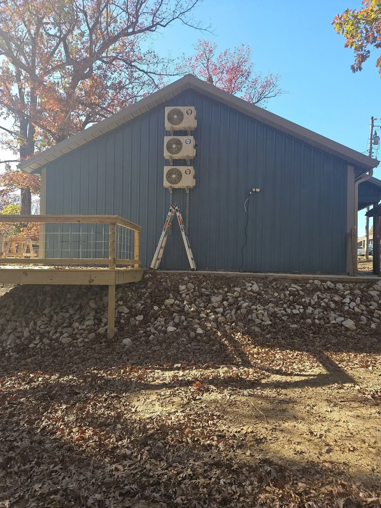 Blue shed with three air conditioning units mounted on the wall. A-frame ladder leans against the building.