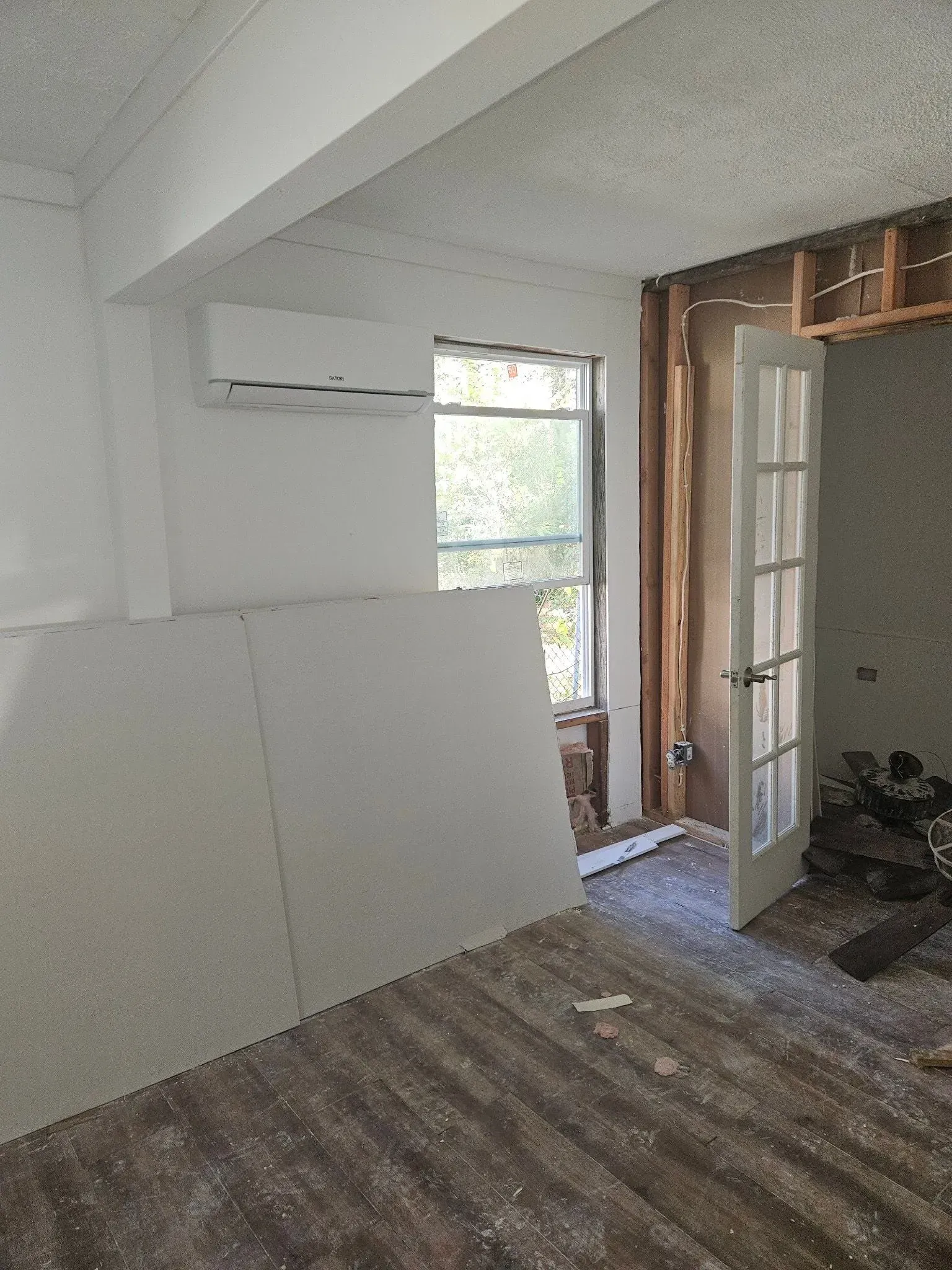 Room under renovation with drywall, window, open door, and air conditioning unit.