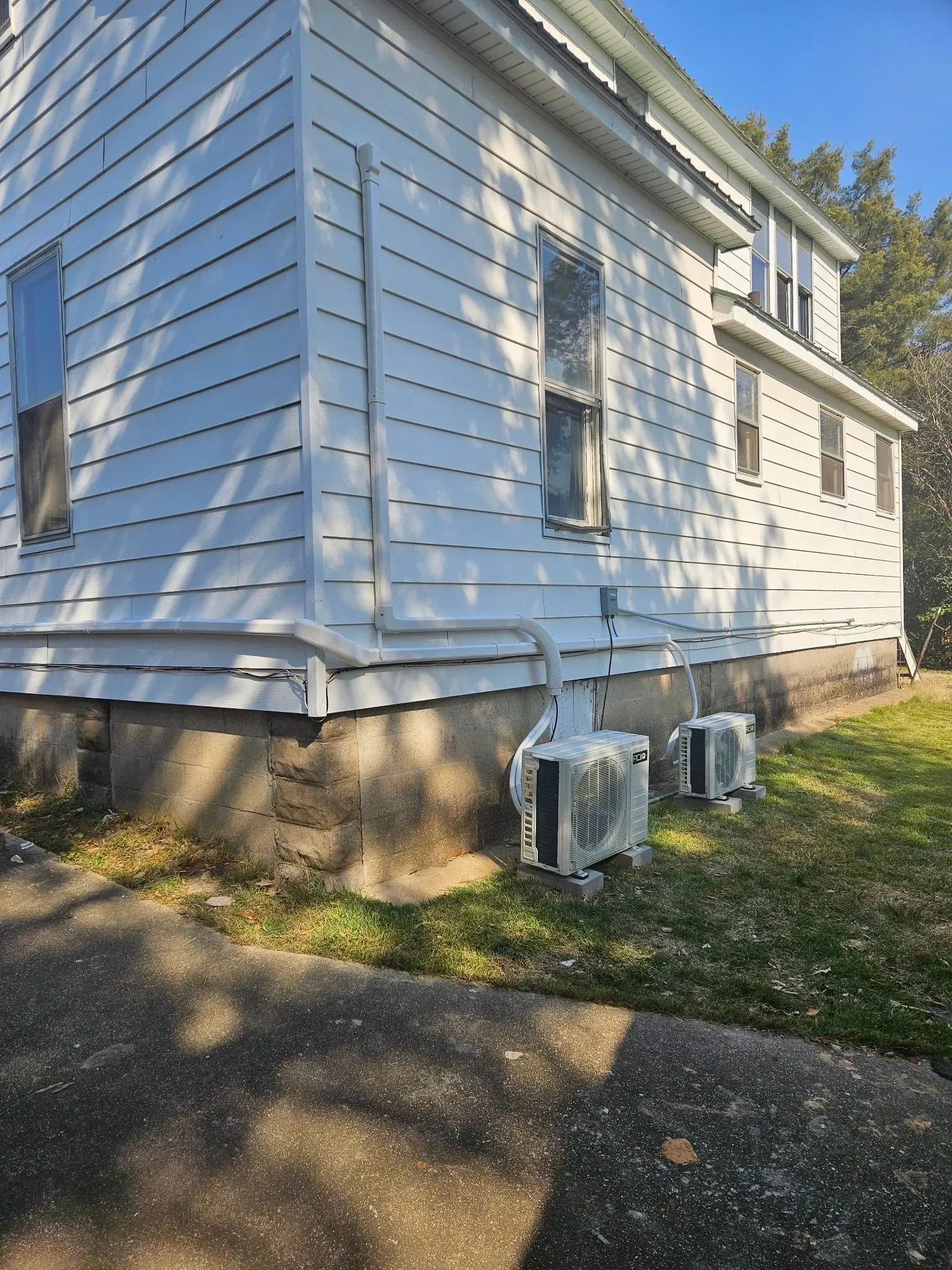 White house with two outdoor air conditioning units on concrete foundation.