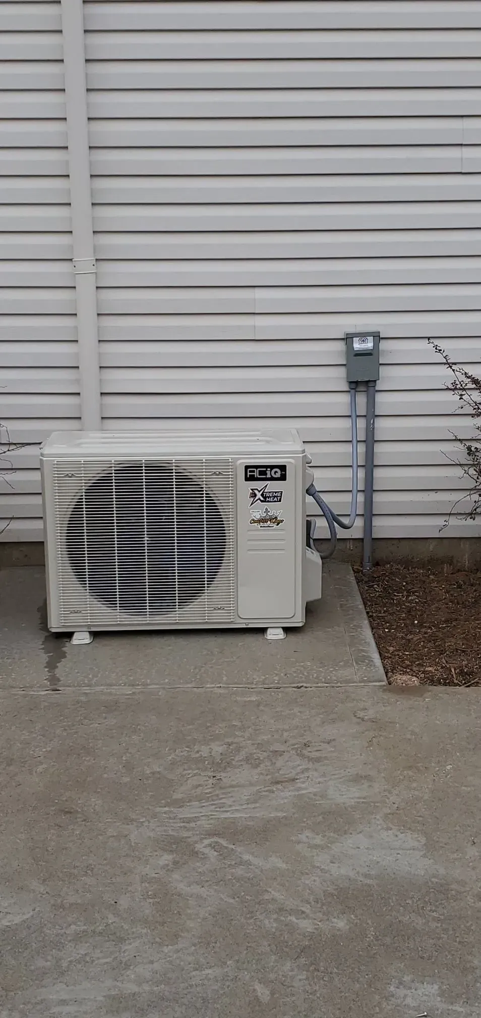 Outdoor air conditioning unit next to a white siding wall.
