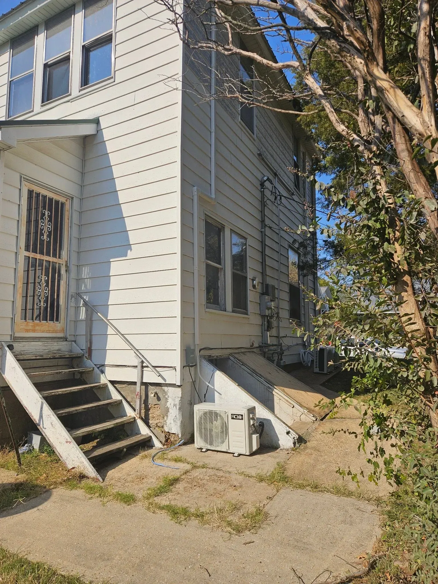 Two-story white house with steps, a security door, and an AC unit outside.